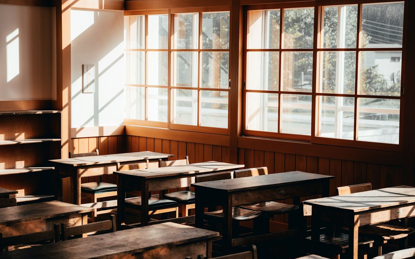 Empty classroom with wooden desks and tall windows in warm light