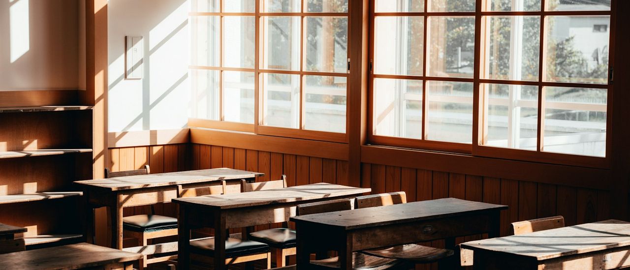 Empty classroom with wooden desks and tall windows in warm light